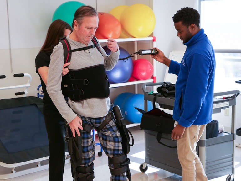 Male patient wearing an exoskeleton device on legs to help him take steps.