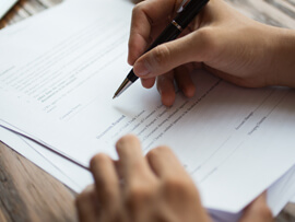A man's hands holding a pen to sign a form.