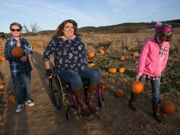 woman in wheelchair with children, picking pumpkins