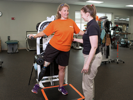 Female rehabilitation therapist works with adult female amputee patient to improve leg strength and balance
