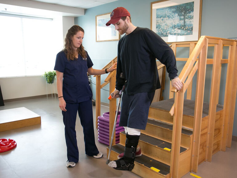 Male patient in leg cast uses stairs to improve mobility during orthopedic rehabilitation therapy session
