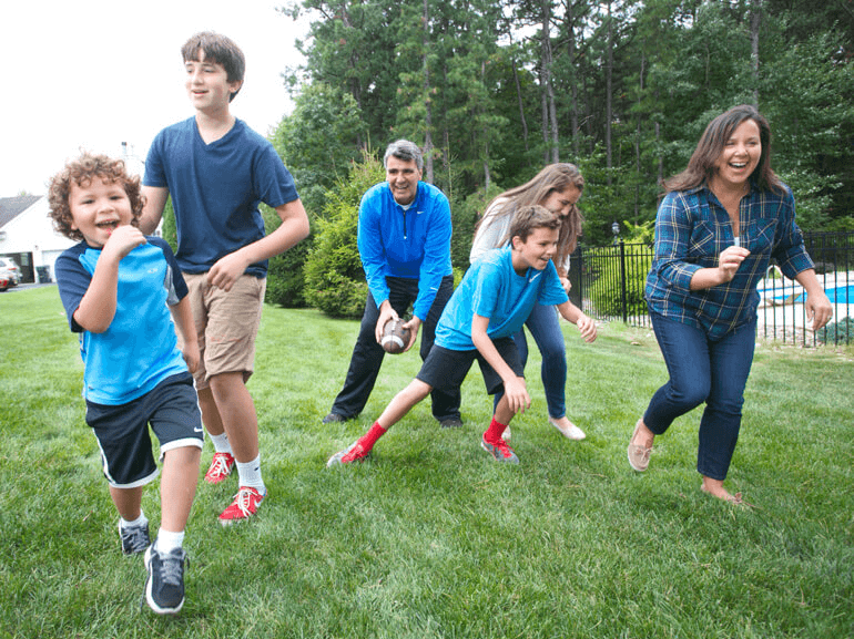 A family of six, all wearing blue clothing, playing football in back yard.