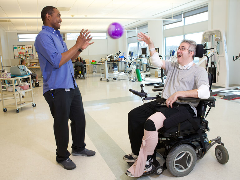 Patient in wheelchair works with therapist using a ball to help range of motion skills rehabilitation