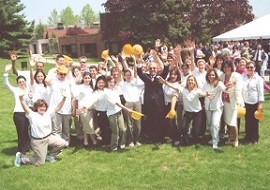 A group of people wearing white shirts with yellow hard hats standing on a grassy lawn.