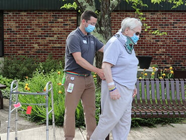 Physical therapist walking behind a man giving him support.