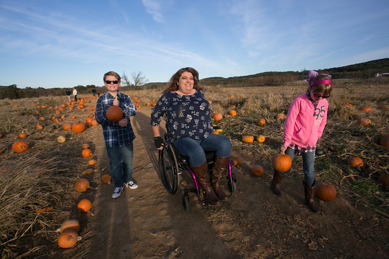 Heather rolling along in her wheelchair through a pumpkin patch on a fall day.