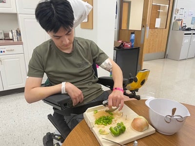 Photo of Junoh Kim using adaptive knives to cut vegetables during a therapy session at Kessler Institute for Rehabilitation.