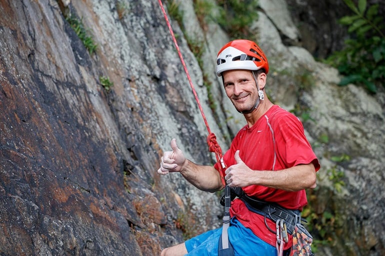 Man wearing climbing gear giving thumbs up sign.