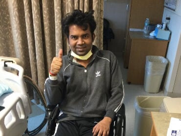 Adesh sitting in a wheelchair in his hospital room giving a thumbs up.
