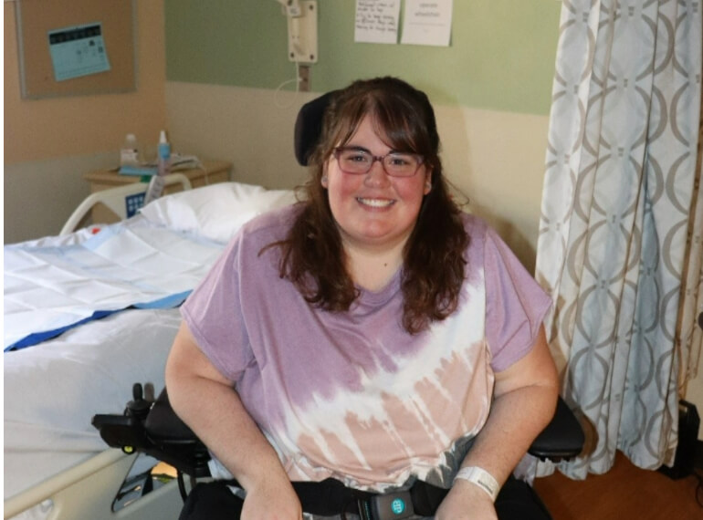 Ashley smiling while sitting in a wheelchair in her hospital room