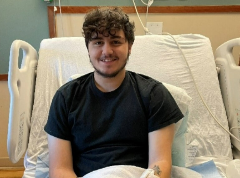Kyle sitting up in his hospital bed smiling with a cast on his left arm.