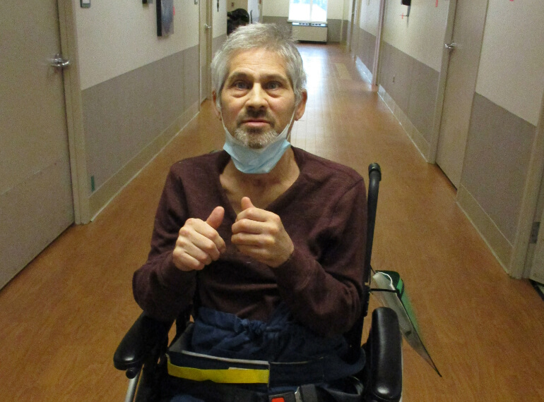 Manuel sitting in a wheelchair in the hospital hallway making a thumbs up.