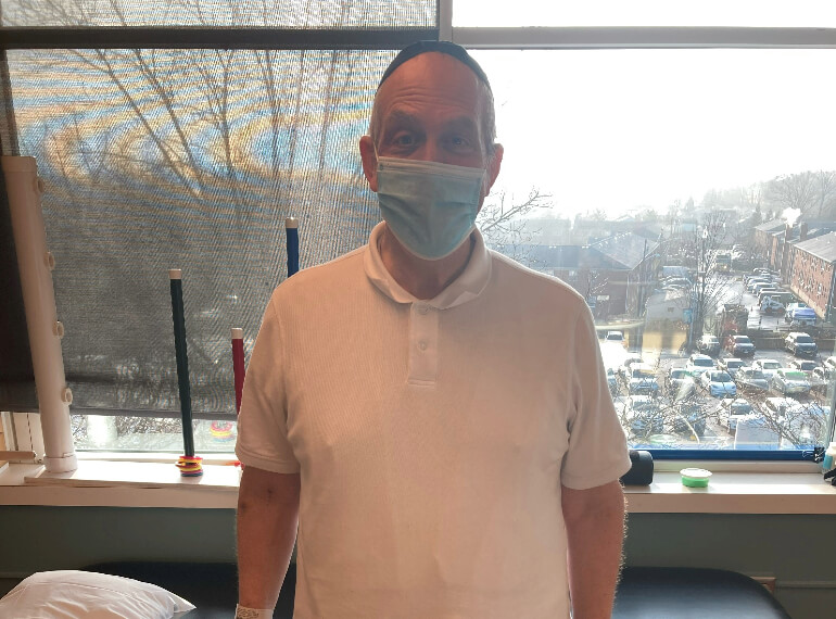 Michael standing in front on the window in his hospital room wearing a mask.