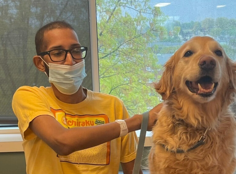Najee sitting with a mask on while petting a therapy dog.