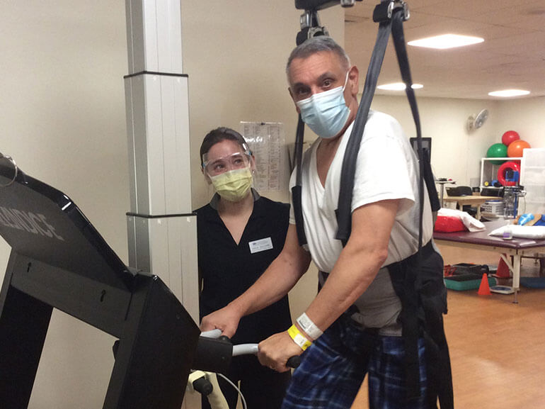 Steven Parisi walking on a treadmill with body-weight support harness wearing a mask.