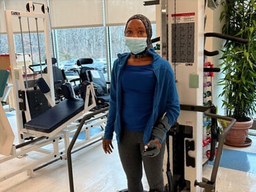 Tiarra standing in the therapy gym with a mask on and arm brace.
