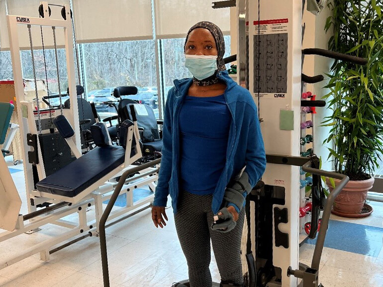 Tiarra standing in the therapy gym with a mask on and arm brace.
